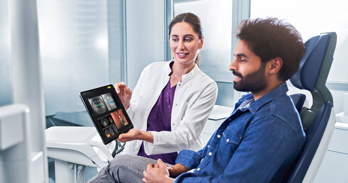 „KI ist wie eine intelligente Zweitmeinung“ Zahnärztin zeigt Patienten im Behandlungszimmer medizinische Röntgenaufnahmen auf einem Tablet.